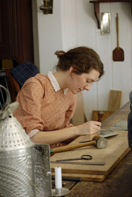 a woman demonstrates working with tin at Black Creek Pioneer Village