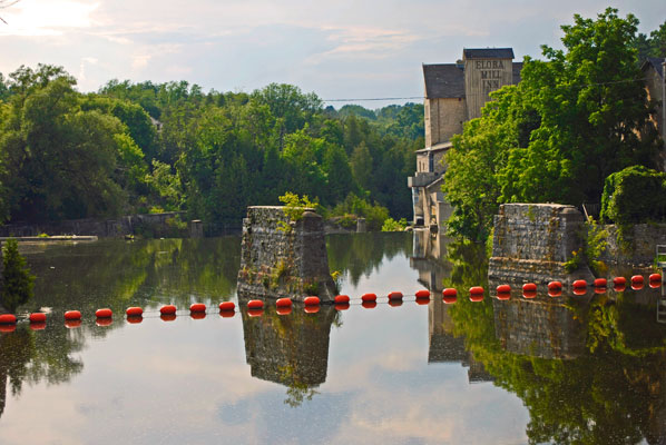 the mill, trees and sky are reflected in the smooth waters of the river in Elora