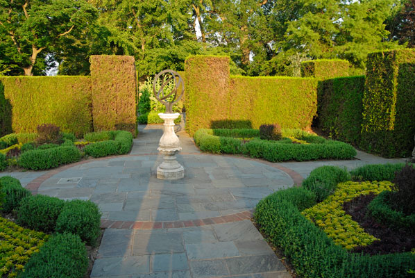 tall hedges surround geometric plantings and a central sculpture in the Herb Garden