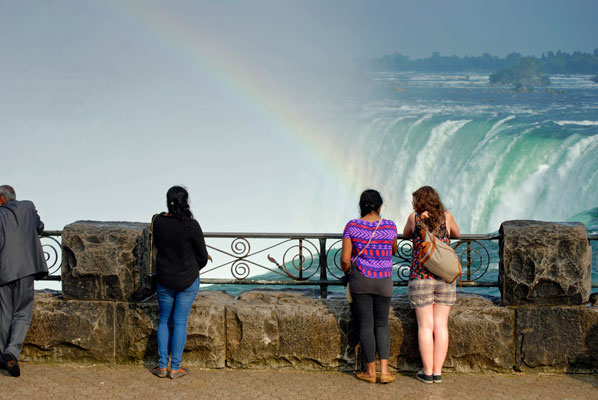 a rainbow glows in the mist above the water as visitors admire Niagara Falls from behind a railing