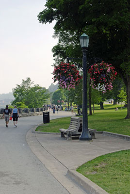 a bench and lamp post with hanging flower pots along the walkway beside the Niagara gorge